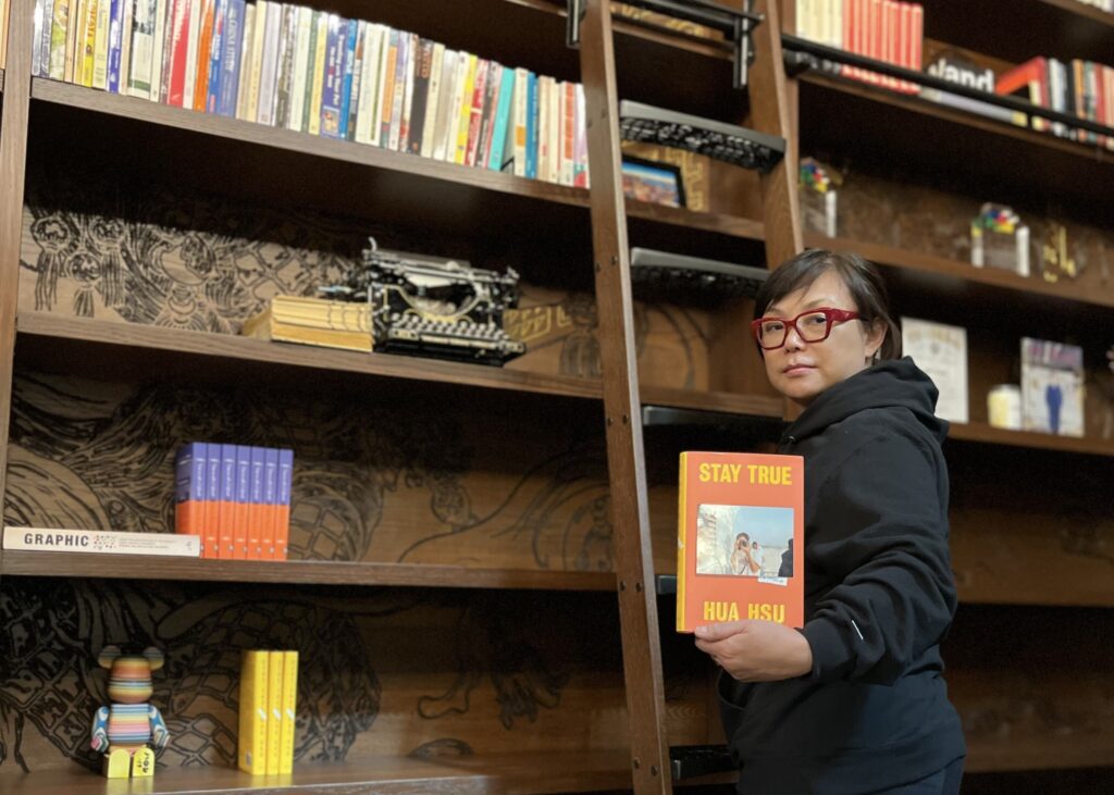 photo of julia huang holding up the book, stay true by hua hsu, in the hand carved library inside intertrend communications